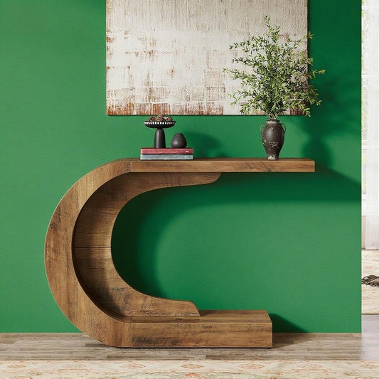Console table curved wooden entry accent table in brown finish with plant vase and books on top against a green wall.