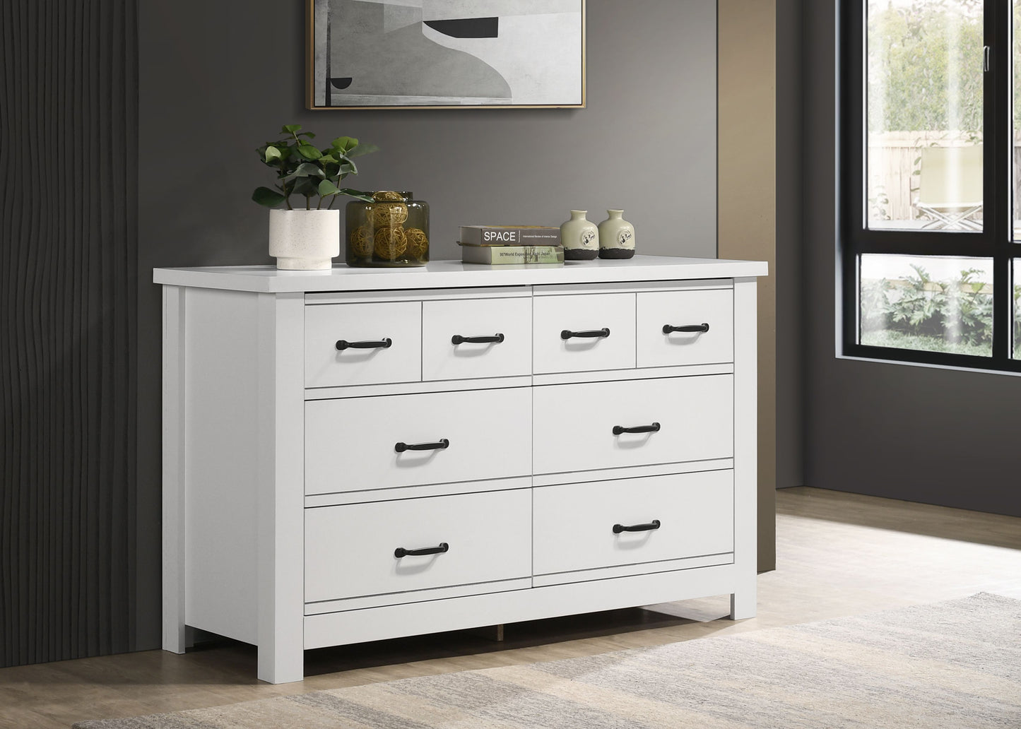 White dresser with multiple drawers and black handles, topped with plant, decorative jar, two books, and two vases.