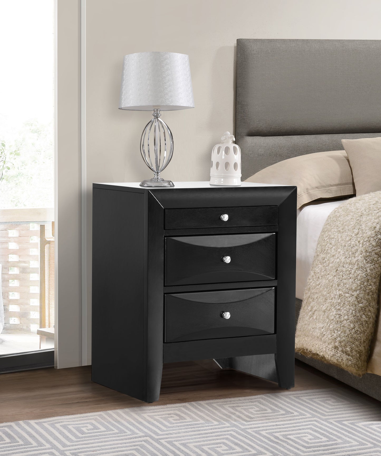 Elegant black nightstand with drawers beside a bed, topped with a silver lamp and white ceramic decor.