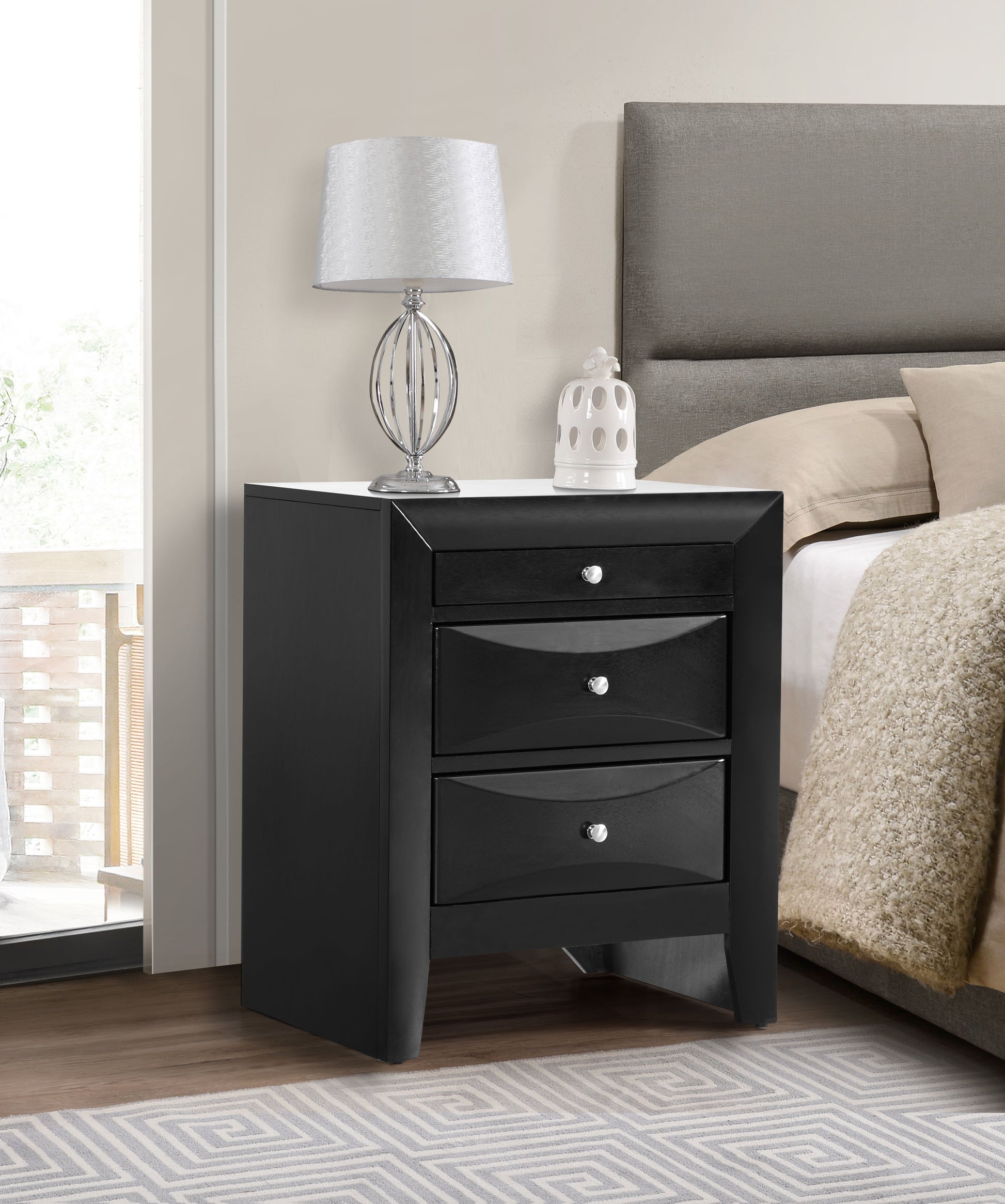 Elegant black nightstand with drawers beside a bed, topped with a silver lamp and white ceramic decor.