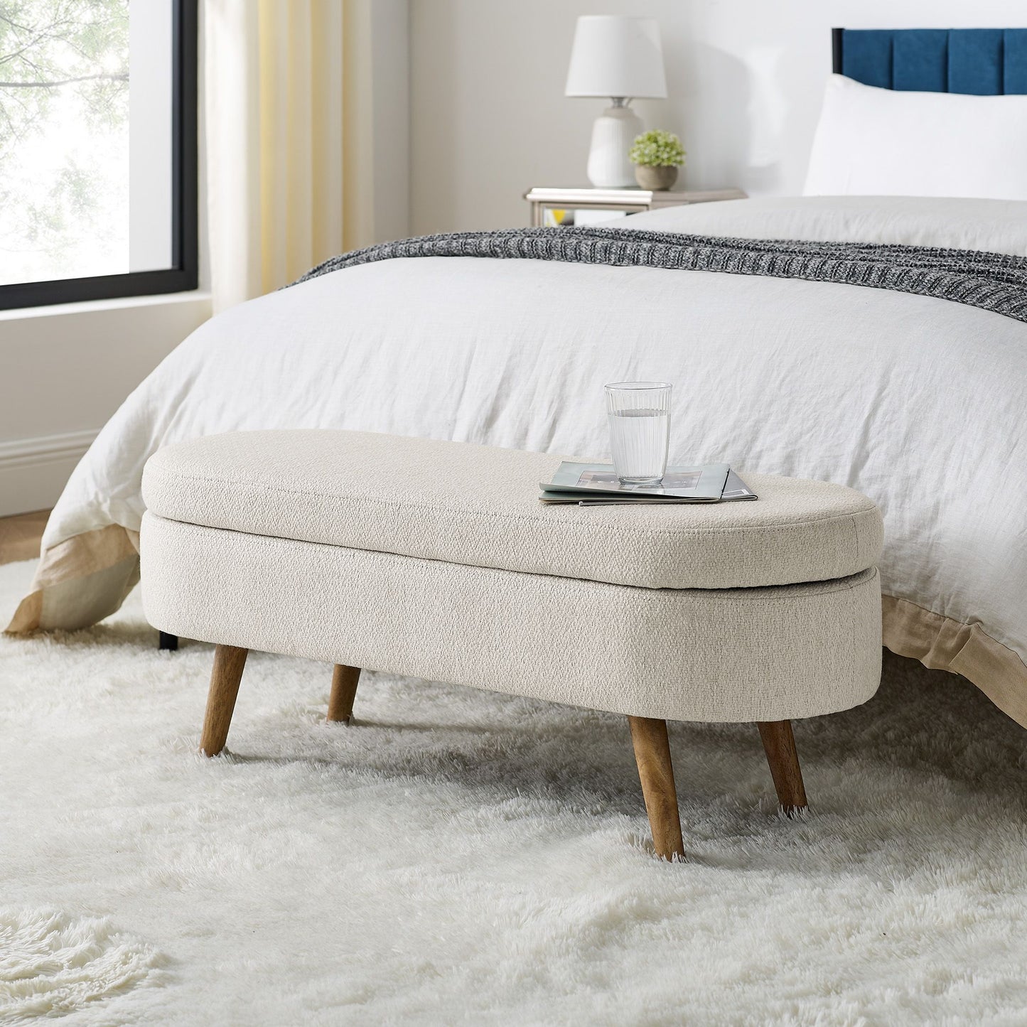 Ottoman oval storage bench, beige fabric with rubber wood legs in a modern bedroom