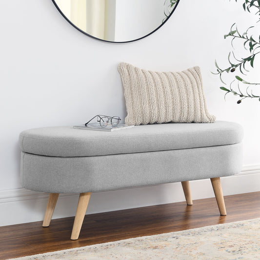 Ottoman oval storage bench with grey fabric upholstery and rubber wood legs.
