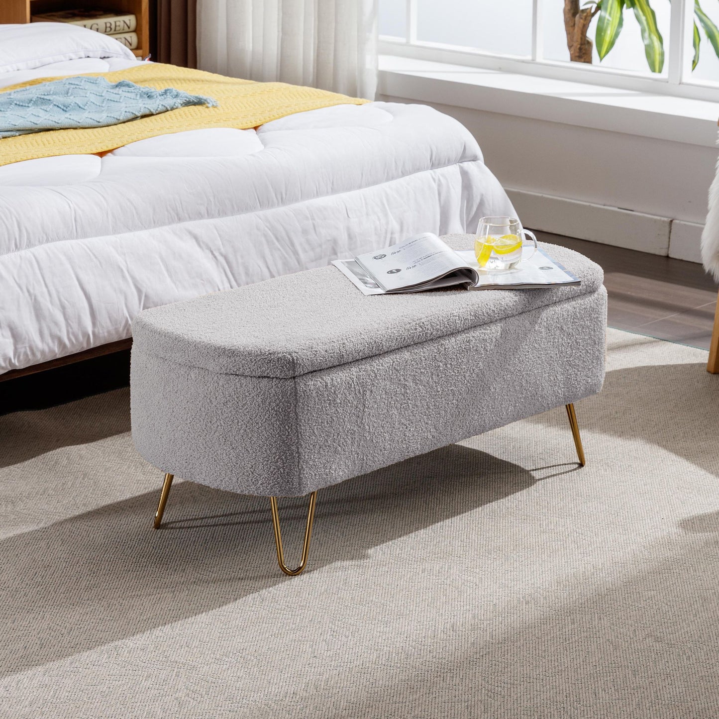 Grey storage ottoman bench with gold legs in a modern bedroom setting