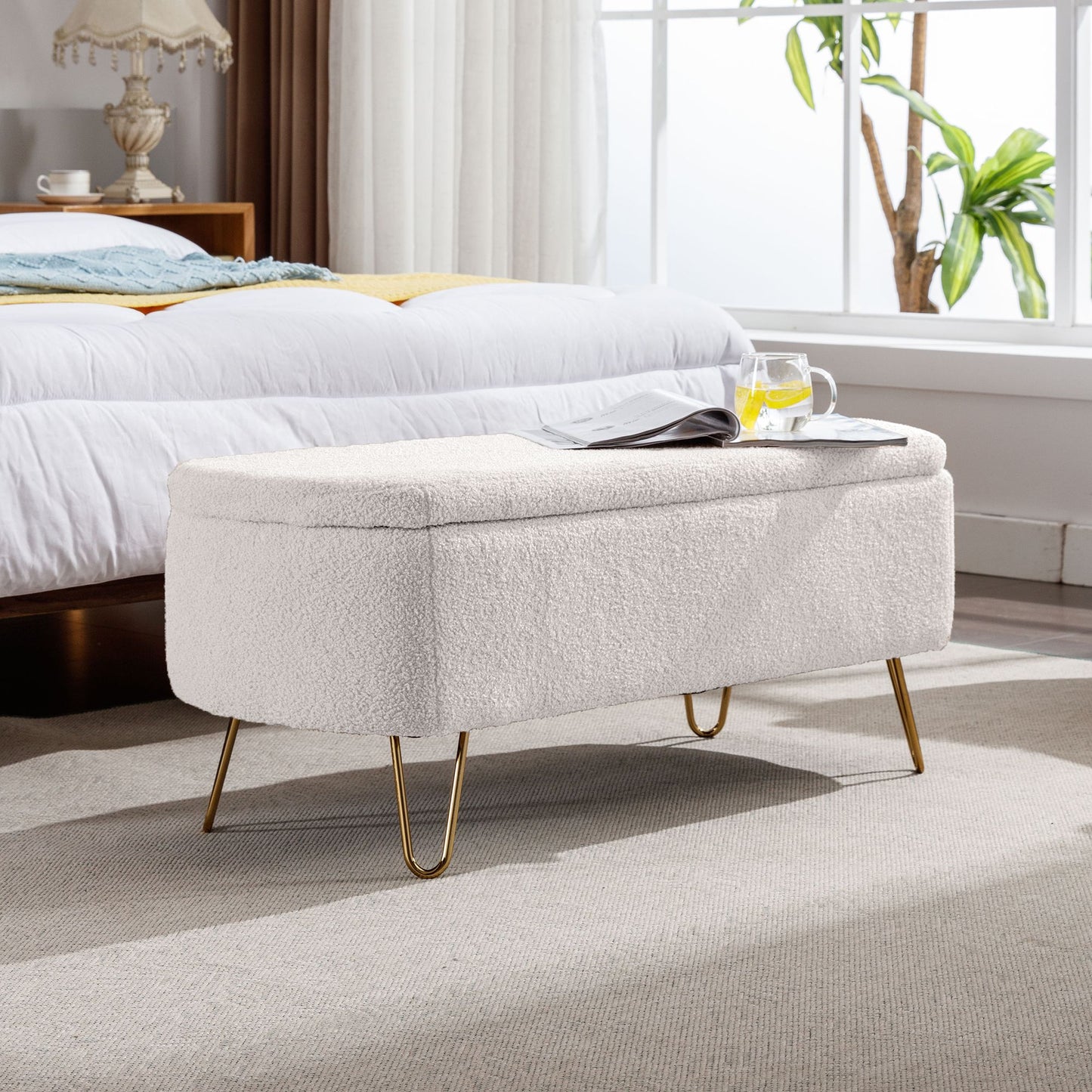 Ivory white storage ottoman bench with gold legs at the end of the bed