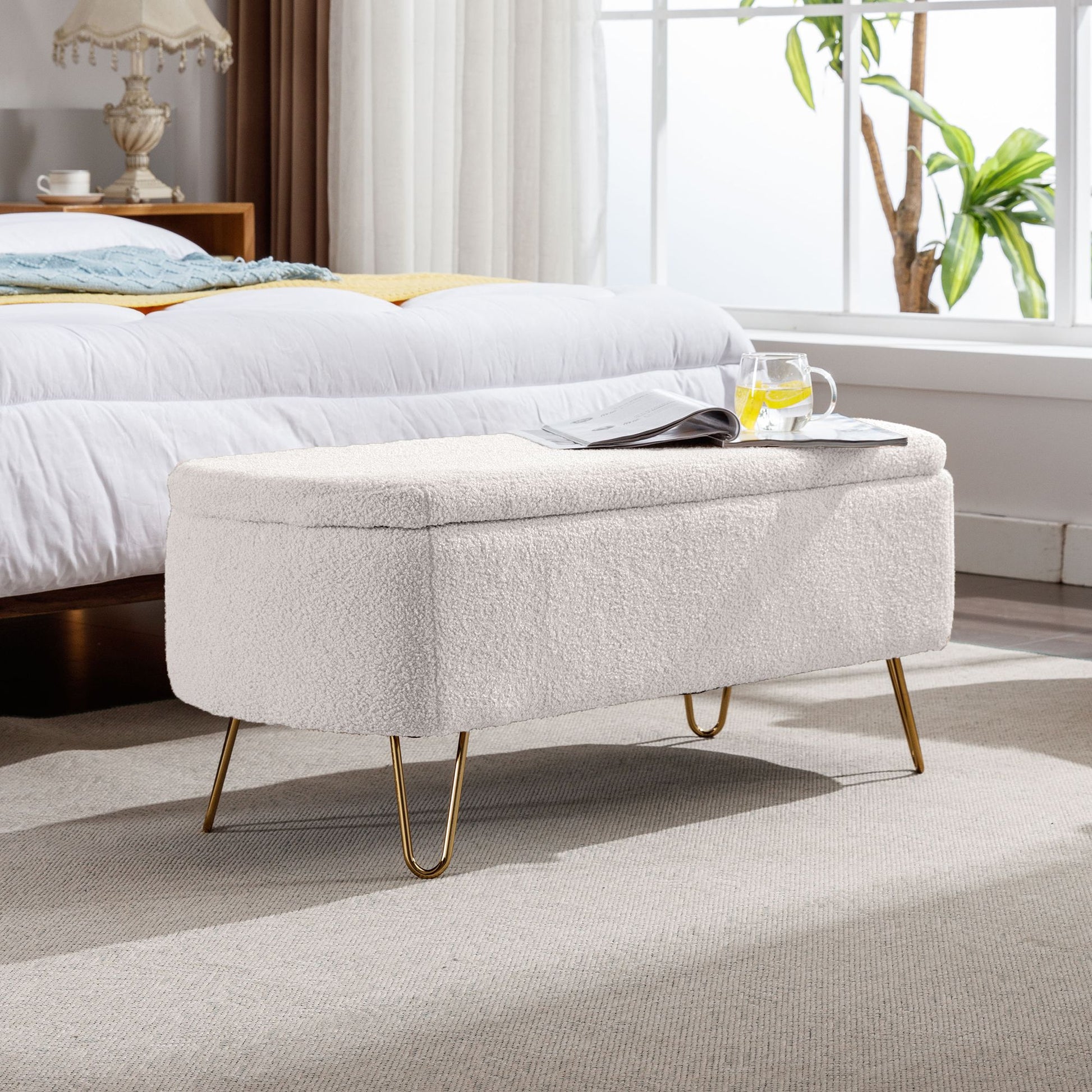 Ivory white storage ottoman bench with gold legs at the end of the bed