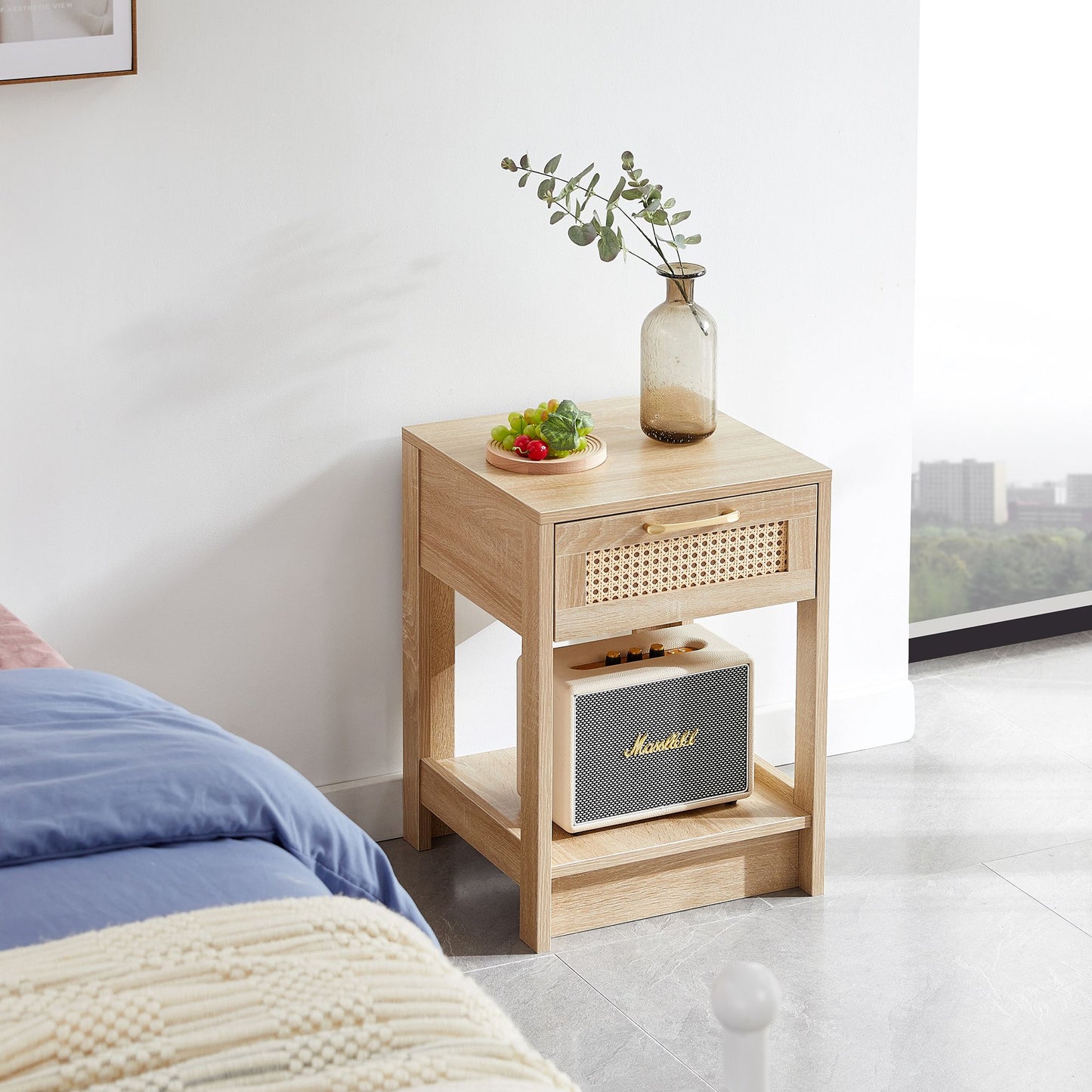 Rattan end table with drawer in natural finish; decor includes a glass vase with eucalyptus and a Marshall speaker.