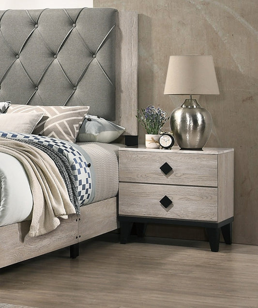Cream-colored plywood nightstand with two drawers and black diamond pulls beside a tufted gray bed