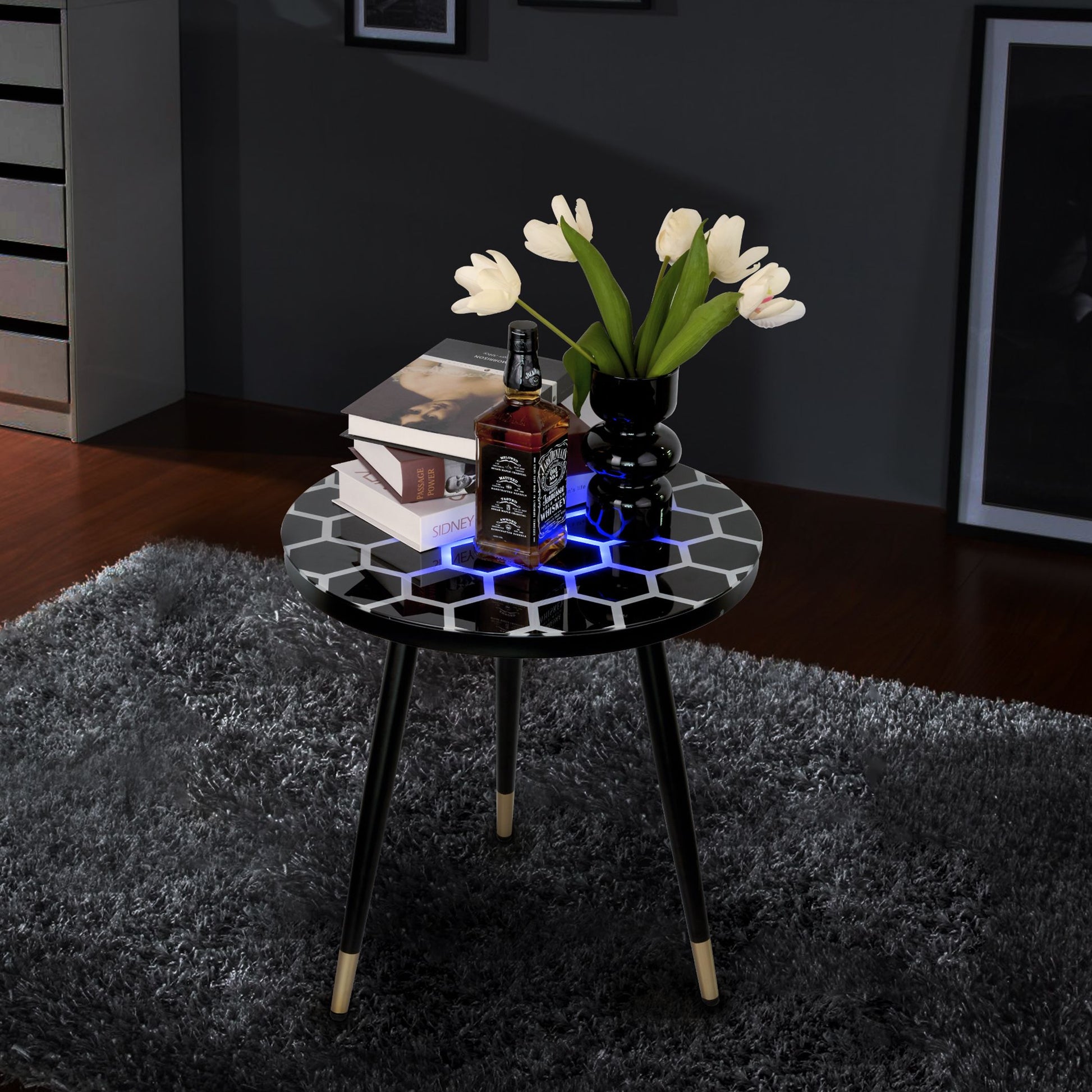 Innovative round LED coffee table with hex and blue glow; books, whiskey bottle, and white flowers in a black vase.