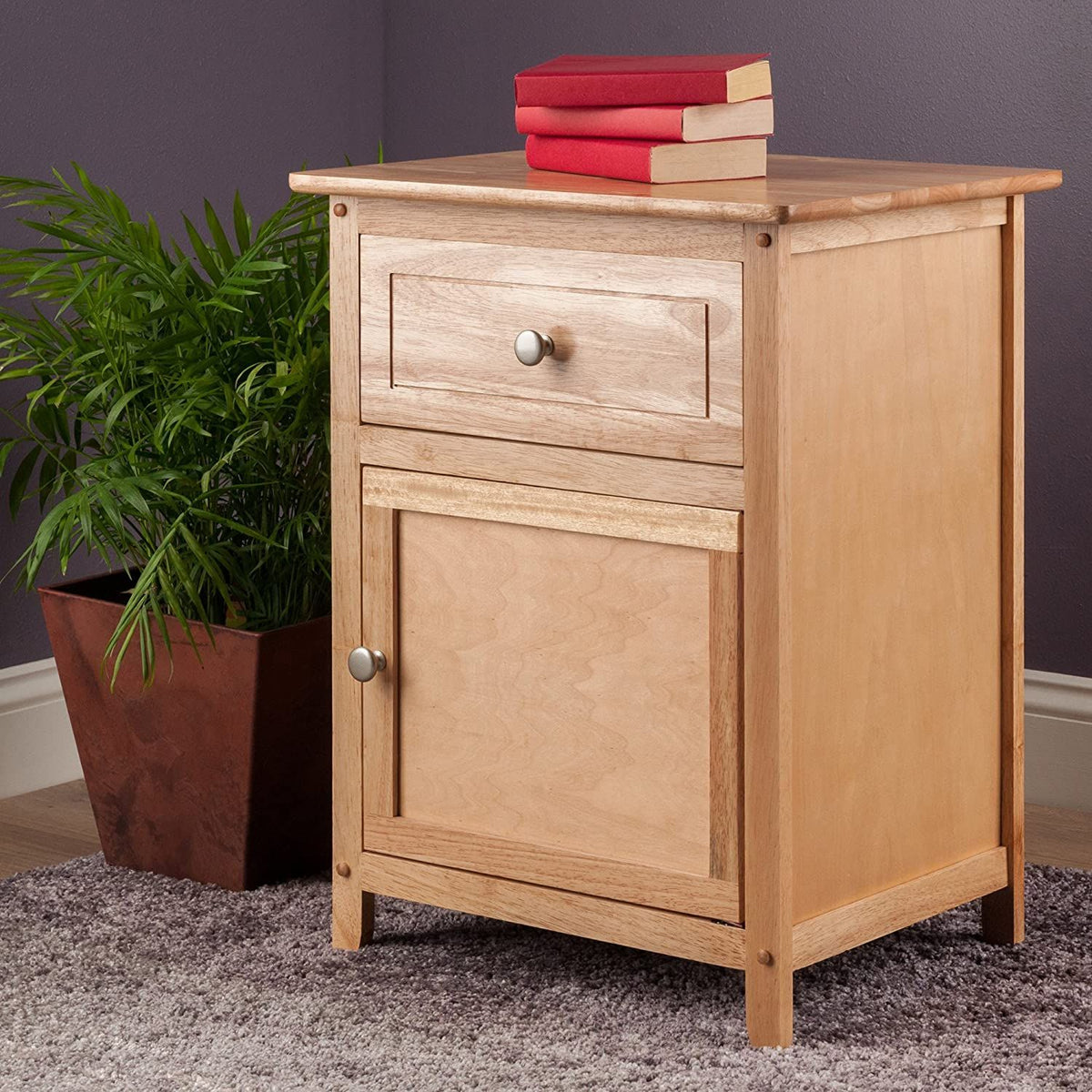 Winsome Eugene Accent Table in natural wood finish with a drawer and cabinet; three red books on top and a plant beside.