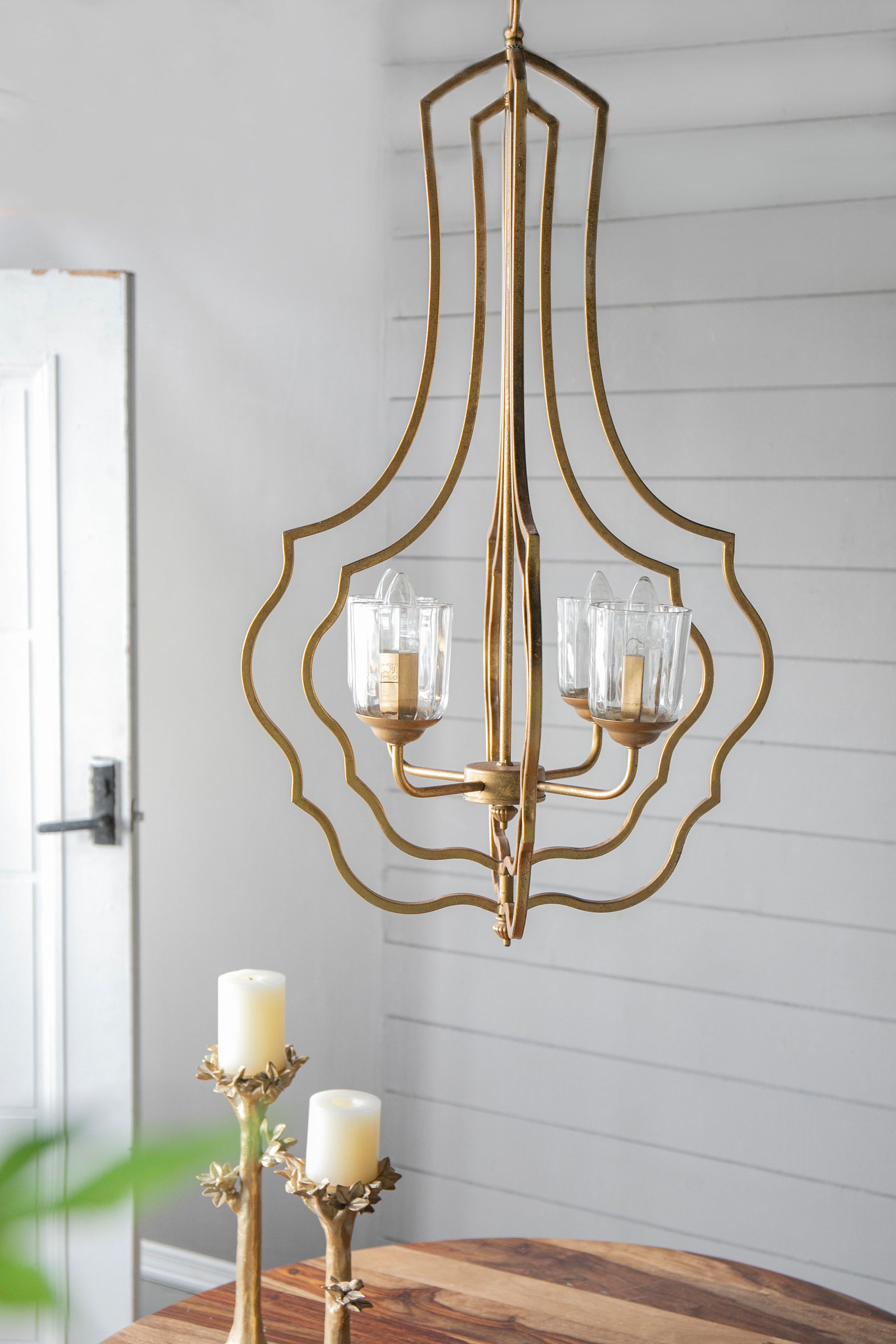 4-light gold metal chandelier with curved open frame and glass candle-style bulbs on an adjustable hanging chain