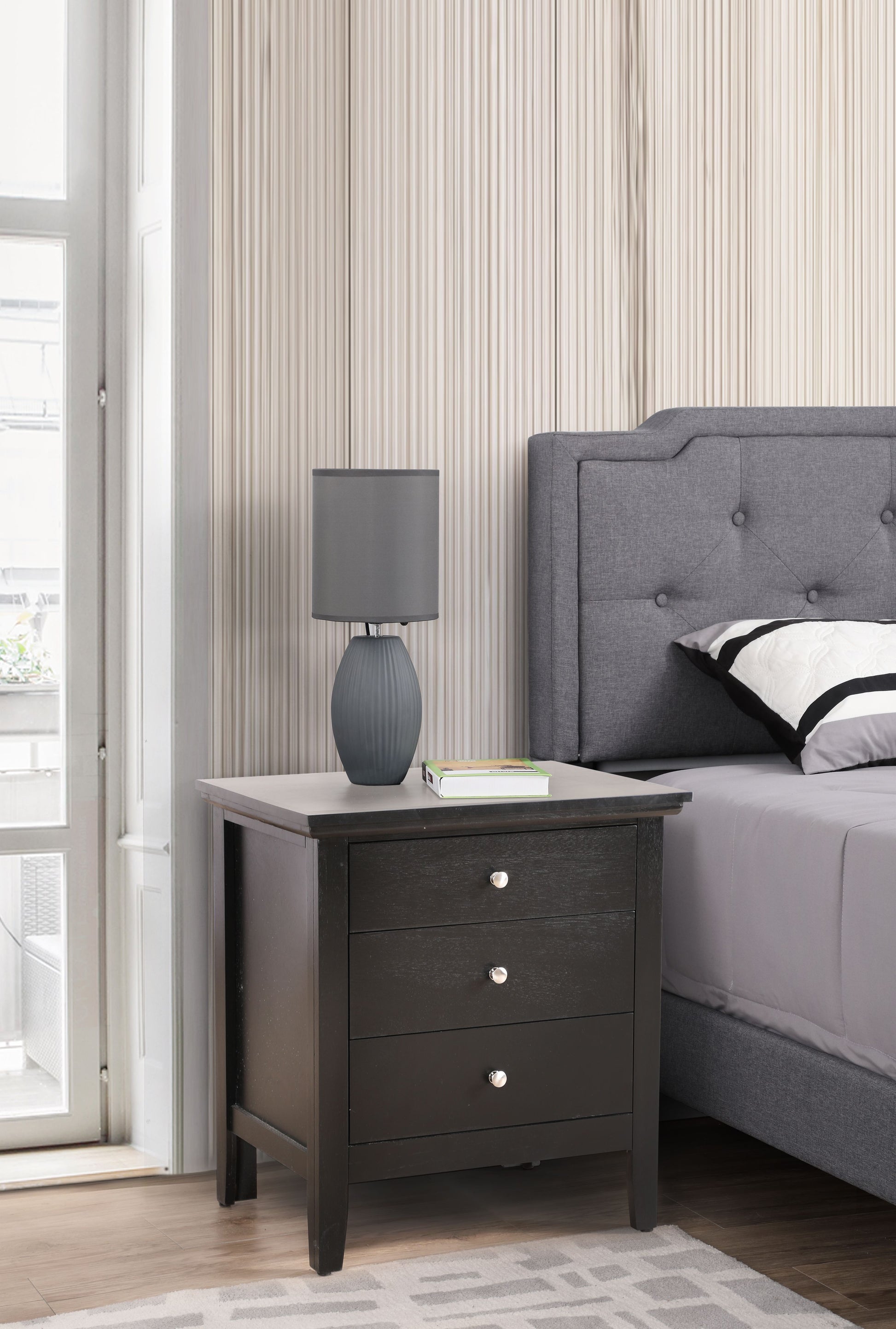Chic black bedside nightstand with three drawers beside a gray upholstered bed